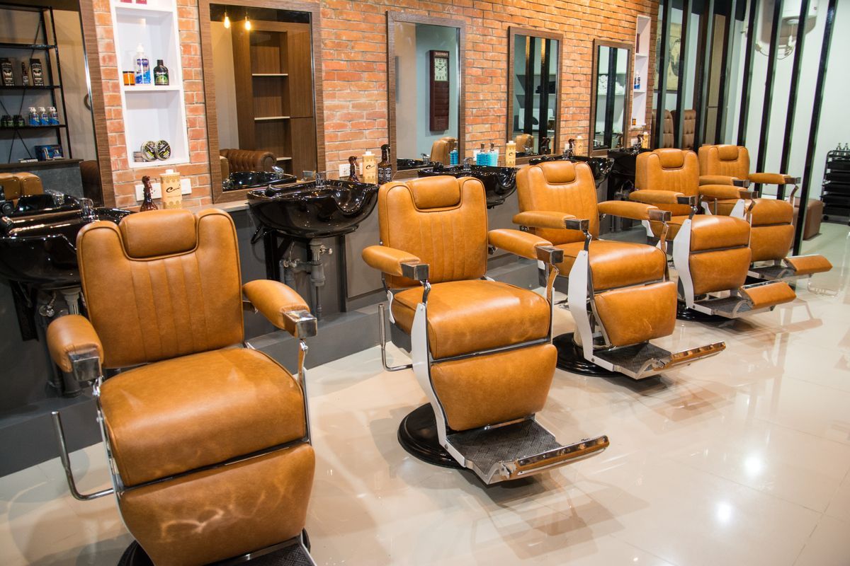 A modern barbershop with a row of brown leather barber chairs facing mirrors and wash basins